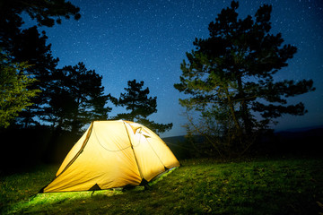 Glowing camping tent in the night mountain forest under a starry sky © MIRACLE MOMENTS