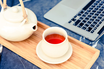 Hot tea is in a glass on a wooden tray near computer