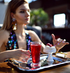 brunette woman in expensive interior restaurant drinking drinking red margarita cocktail and eat dessert cake with strawberry 