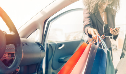 black girl with shopping bags entering in car while  using smart phone