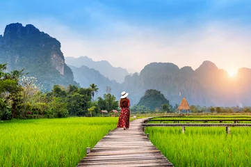 Foto op Canvas Young woman walking on wooden path with green rice field in Vang Vieng, Laos. © tawatchai1990