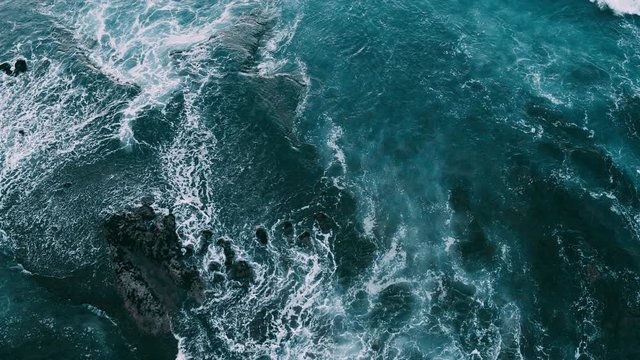 Abstract aerial view of moody ocean waves crashing on rocky shoreline 