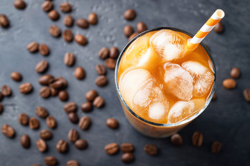 Ice coffee in a tall glass with cream poured over, brown sugar and coffee beans. Cold summer drink on a dark background.