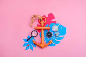 Colorful travel and vacation concept on a bright pink background. Tropical leaves, wooden anchor, compass and sea shells with copy space.