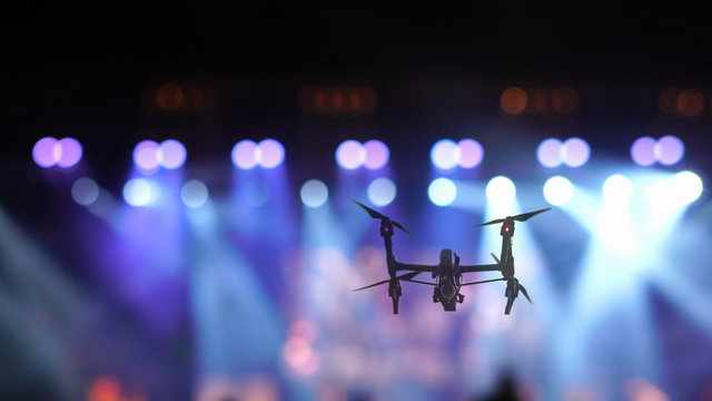 Closeup Silhouette Of Drone Flying For Taking Video Of Concert Crowd And Abstract Blurred Photo Of Spotlight In Conference Hall, Musical And Concert Concept