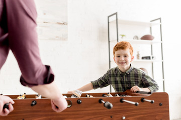 cropped shot of father and cute smiling son playing table football together at home