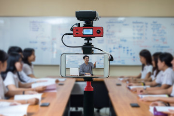 Closeup smart mobile phone taking Live of Asian teacher in the classroom,Camera for photographer or Video and Technology Live Streaming concept,University education