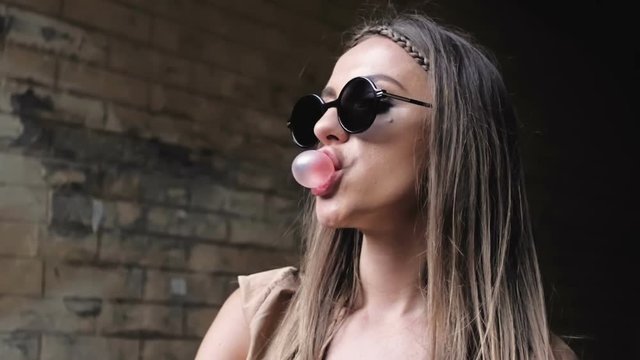 Closeup slow motion footage of stylish young woman chewing bubble gum and blowing bubbles