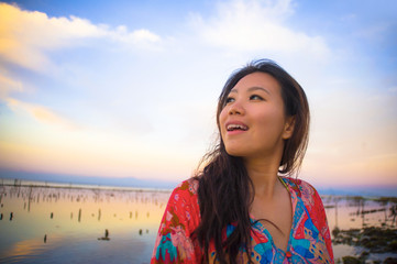 young happy and beautiful Korean woman in traditional Asian dress at sunrise sea landscape looking away thoughtful and pensive in relax enjoying
