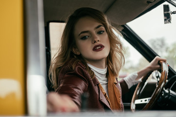 selective focus of attractive girl holding steering wheel of classic car