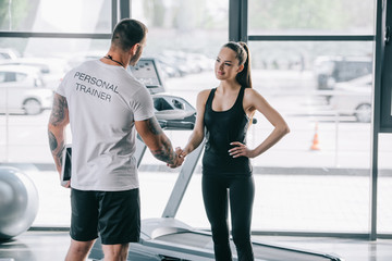 rear view of male personal trainer and young sportswoman shaking hands at gym - obrazy, fototapety, plakaty