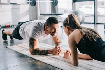 Schilderijen op glas male personal trainer and sportswoman doing plank at gym © LIGHTFIELD STUDIOS