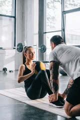 Fotobehang male personal trainer helping sportswoman to do abs with ball at gym © LIGHTFIELD STUDIOS