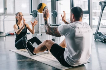Deurstickers male personal trainer and sportswoman doing exercises with ball at gym © LIGHTFIELD STUDIOS
