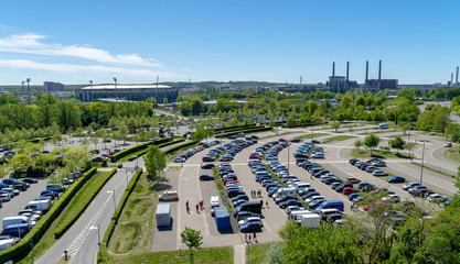 Aerial view over a large parking lot with many parked cars onto a football stadium and the factory