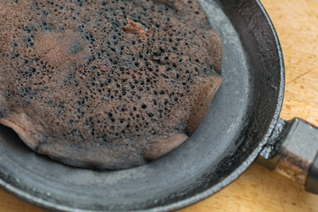 Scorched pancake close-up in a frying pan and wooden stand