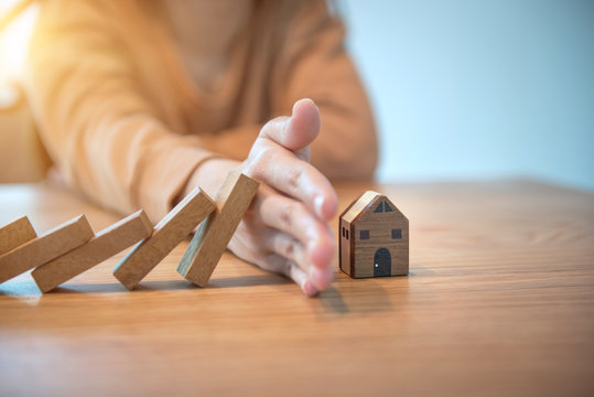 Woman hand stopping risk the wooden blocks from falling on house, Home insurance and security concept.