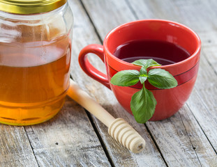 Obraz na płótnie Canvas Red cup of tea, basil leaf and honey on white wood