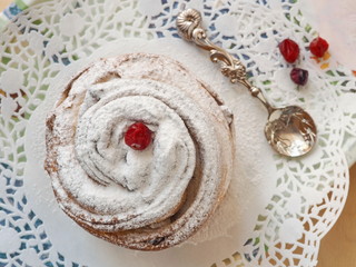 Top view of cruffin dessert decorated with sugar powder. Fresh muffin upon white doily with cute teaspoon and red berries. Selective focus.