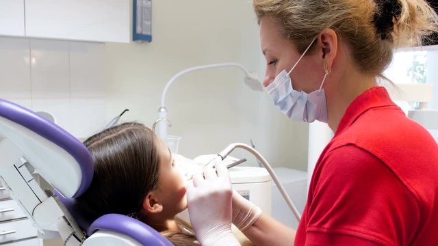 Closeup 4k footage of dentist treating girl's teeth and removing caries
