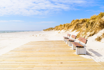 Sandhammaren, Sweden - Three benches on a wooden platform at the sandy beach on a sunny day.