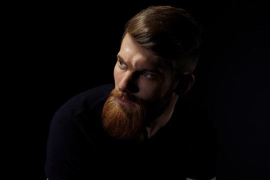 Image of single standing in profile young handsome serious bearded man over black background with copy space.