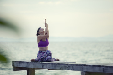 woman playing yoga on wooded pier against plain sea background