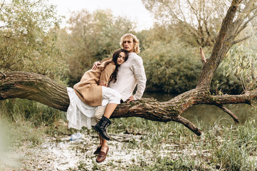A beautiful couple in the boo style embraces sitting on a branch over the lake