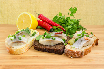 Three different open sandwiches with pickled herring on wooden surface