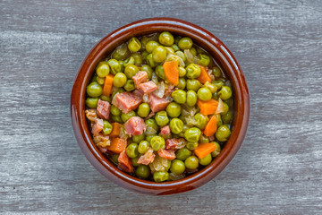 Peas with ham in a clay pot on a worn wooden table. Top view.