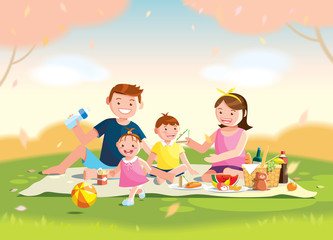 Family enjoying picnic. They are sitting on the grass in a park, the basket with meal and toys for the kids. Blurred background. 
