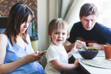 Cute funny baby boy 2 years old sitting at the table with parents, family breakfast
