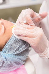 Close up of hands of young cosmetologist injecting botox in female face