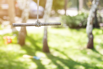 Fototapeta premium Wooden single rope swing in garden on bright sunny day. Green grass lawn on background. Children having fun and summer activity concept