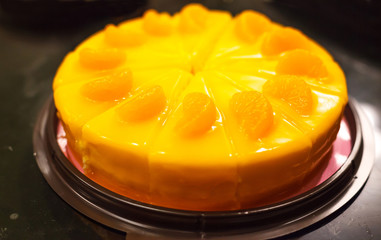 selective focus on bakery dessert, orange color cake with orange mousse and orange fruit toppings on black glass table background
