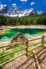 Big rock and green mountain Carezza lake in Dolomites, Italy