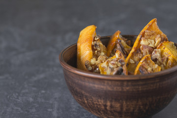 Authentic view of the baked sliced pumpkin with honey and walnuts in a ceramic bowl (pial) on a dark gray background.