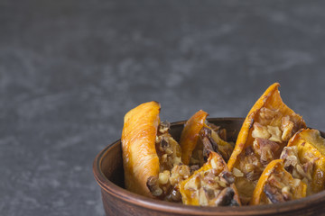 Authentic view of the baked sliced pumpkin with honey and walnuts in a ceramic bowl (pial) on a dark gray background.
