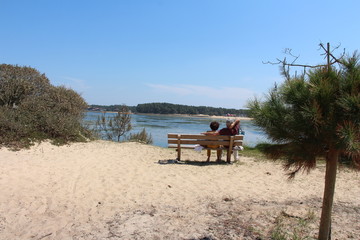 Fototapeta na wymiar Couple de vacanciers assis sur un banc de dos regardant le lac par temps ensoleillé