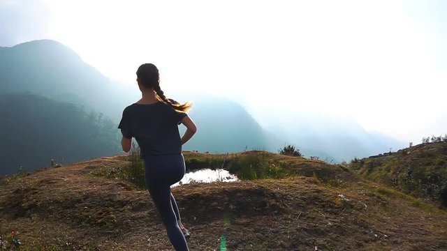 Runner woman jogging on cliff at sunrise with amazing view on mountain range