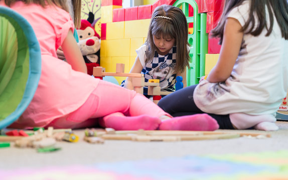 Cute pre-school girl looking down with concentration while building a structure from wooden toy blocks during playtime in a modern kindergarten