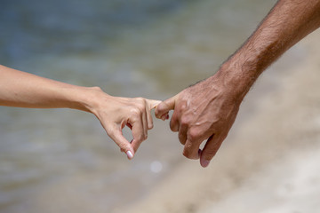 Summer couple holding hands on beach. Romantic young couple enjoying sun, sunshine, romance and love by the sea.