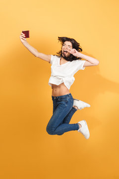 Emotional woman jumping make selfie by mobile phone with peace gesture.