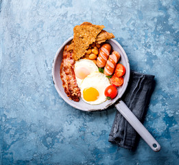 Traditional English Breakfast in the Frying Pan  Food on the Blue Background. Eggs, Sausages, Bacon, Beans,Toasts,Coffe and Orange juice Copy space for Text