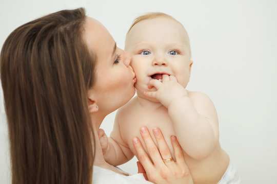 Mother kisses her child, baby holds his finger near mouth