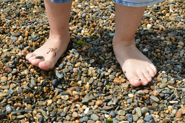 The child walks barefoot on the pebbles of the black sea coast.