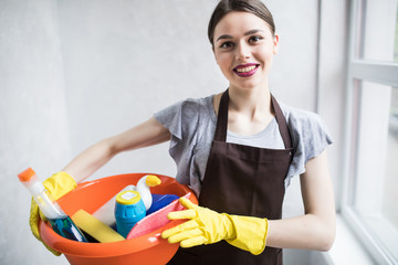 Young pretty woman with tools. Woman with detergent basket before cleaning at home. House cleaning service concept.