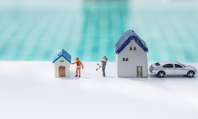Property and real estate business concept, miniature couple and worker with small house over blurred blue water background