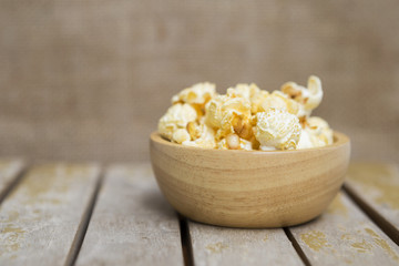 Salted popcorn in wooden bowl over blurred hessian texture background, movie snack, unhealthy food