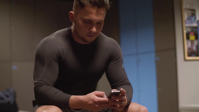 Tired man using mobile phone at locker room/